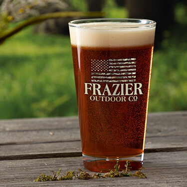 A675 American Outdoor Company - American flag in a camouflage motif above Your Name, Outdoor Company on a color printed pint glass.