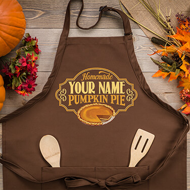 A699 Pumpkin Pie - Homemade Your Name Pumpkin Pie above a sliced pumpkin pie on a brown apron.