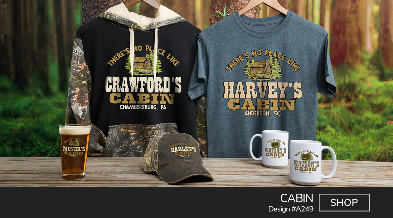 A249 | Cabin - There's No Place Like Your Name Cabin, Your Location, around a classic log cabin flanked by pine trees on a blue tee, 2 tone camo hoodie, 2 tone camo baseball hat, color printed pint glass, and ceramic coffee mugs.