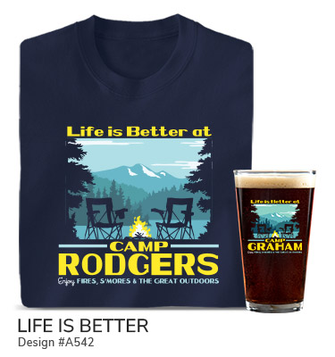 A542 | Life Is Better - Life Is Better At Camp Your Name, Enjoy Fires, S'mores, and The Great Outdoors, around trees, camp chairs, and a campfire by a lake with a mountain in the distance, on a navy T shirt and color printed pint glass.